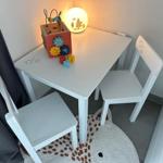 Kindertisch mit zwei Stühlen und Spielzeug auf weißem Tisch.