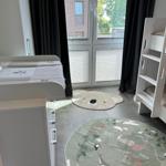 Zimmer mit Kinderbett, Doppelbett und zwei Teppichen. Fenster mit Jalousien und Vorhängen.