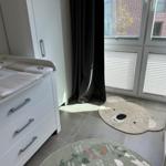 Kinderzimmer mit Wickelkommode, Bären-Teppich und Fenster mit Jalousien.