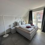 Schlafzimmer mit Doppelbett, Nachttisch und Kleiderständer. Fenster mit Vorhängen.