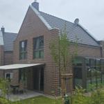 Moderne Villa mit Garten und Terrasse. Glasveranda und Holztisch sichtbar.
