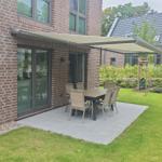 Terrasse mit Tisch und Stühlen unter Markise. Grünfläche und Gartenhaus im Hintergrund.