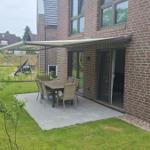 Terrasse mit Tisch und Stühlen unter Markise. Grünflächen und Gartenbereich.