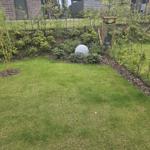 Garten mit Rasenfläche, Blumenbeete und kleinem Steinobjekt.