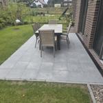 Terrasse mit Tisch und Stühlen neben Haus mit Garten.