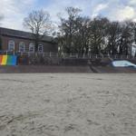 Strand mit gemalter Wal und Regenbogenwand vor einer Backsteinhütte.