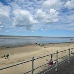 Strand mit Watt, Menschen, Steg und blauem Himmel mit Wolken.