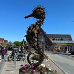 Große Metallskulptur eines Seepferdchens vor einem Markt und Fahrradstellplatz.