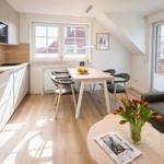 Wohnküche mit Esstisch, Sofa und Fenstern. Holzboden und moderne Einrichtung.