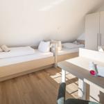 Zimmer mit zwei Betten, Schreibtisch und Kleiderschrank. Holzfußboden und Dachschrägen.