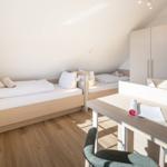 Zwei Betten, Schreibtisch und Kleiderschrank in einem Dachzimmer mit Holzboden und Fenster.