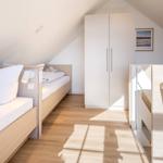 Zimmer mit zwei Betten, Schrank und Tisch unter schrägen Dachdecken.