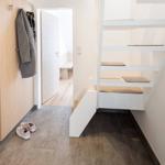 Hausflur mit Treppe und Schuhen an der Wand. Tür führt in das Schlafzimmer.