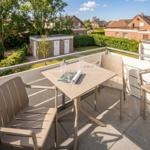 Terrasse mit Tisch und vier Stühlen. Blick auf Grünflächen und Nachbarhäuser.