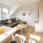 Wohnbereich mit Sofa, Esstisch und Küchenzeile. Große Fenster und Holzboden.