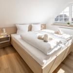 Schlafzimmer mit Doppelbett, Holzboden und Fenster mit Blick auf Dächer.