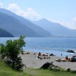 Strand mit Menschen, Boot und Bergen am See.