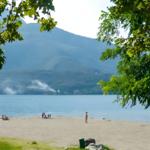 Strand mit Menschen, See und Bergen im Hintergrund