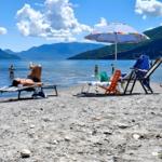 Strand mit Liegestühlen und Sonnenschirm am See. Menschen baden und sonnen sich.