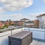 Terrasse mit Blick auf Wohnhäuser und Himmel. Holzbox und weißer Geländer.