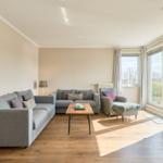 Wohnzimmer mit Sofa, Sessel und TV. Holzboden und große Fenster.