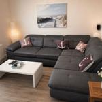 Wohnzimmer mit grauem Ecksofa, weißen Couchtisch und Seeblick-Bildern an der Wand.