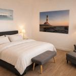 Schlafzimmer mit Bett, Sessel und Wandbildern von Leuchtturm und Schiffen.