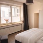 Schlafzimmer mit Bett, Fensterbank und Spiegel. Ein dunkler Sessel und eine Lampe sind sichtbar.