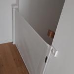 Weißes Babygitter an Wand, Holzregal mit Bild und Kerzen darüber.