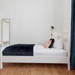 A bedroom with a white bed, wooden floor, and blue curtains.