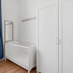 A room with a white crib, a mirror, and a white wardrobe.