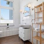 Bathroom with toilet, sink, and wooden shelf with towels.