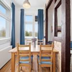 Dining area with wooden table, blue chairs, and windows. Living area with sofa in background.