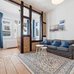 Living room with sofa, rug, and wooden floor. Passage to dining area with wooden chairs.