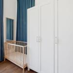 Childs room with crib, white wardrobes, and blue curtains.