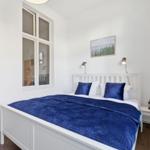 A bedroom with a white bed, blue bedding, and a window.