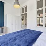 Bedroom with bed, blue cover, white walls, and windows. A wardrobe is against the wall.