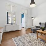 Living room with wooden floor, window, armchair, sofa, table, and rug.