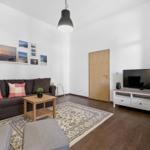 Living room with sofa, TV, and wooden floor. Wall art and rug visible.
