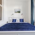 Bedroom with white bed, blue quilt, and two windows.