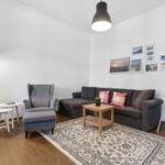 Living room with sofa, armchair, table, and rug. Wall art and floor lamp.