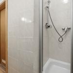 Bath with shower, tiled wall, and wooden door. Hand shower and shower rail visible.