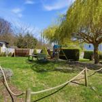 Backyard with playground, table, chairs, and large tree.