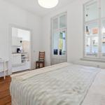 Bedroom with bed, wooden floor, and window. Kitchen visible in background.