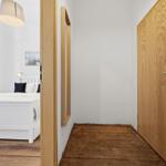Bedroom with white bed and wooden floor. Door and mirror on the wall.
