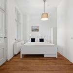 Bedroom with white bed, wooden floor, and window. Pendant lamp and wall picture visible.