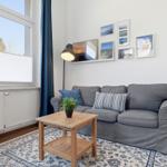A living room with a gray sofa, wooden table, and window overlooking a house.