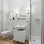 Badezimmer mit Dusche, Waschbecken und Toilette. Fliesenwand und Holzboden.
