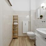 Badezimmer mit Toilette, Waschbecken und Holzregal an der Wand.