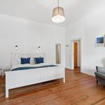 Schlafzimmer mit weißem Bett, Holzboden und grauer Sessel.